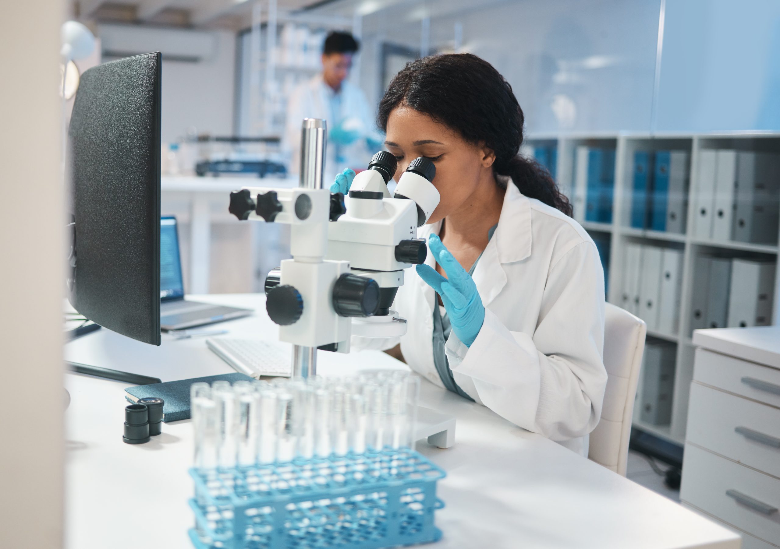 Shot of a young female lab worker analysing samples through a microscope.